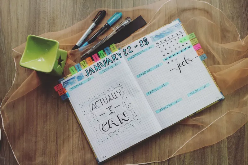 Una agenda abierta con la semana rotulada a mano y marcadores de colores.